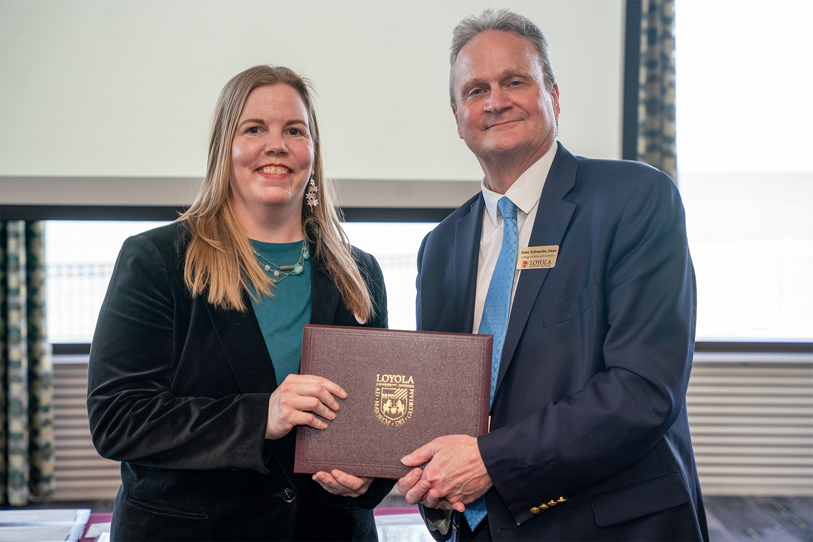 blonde woman in teal accepts award from man in grey suit with blue tie